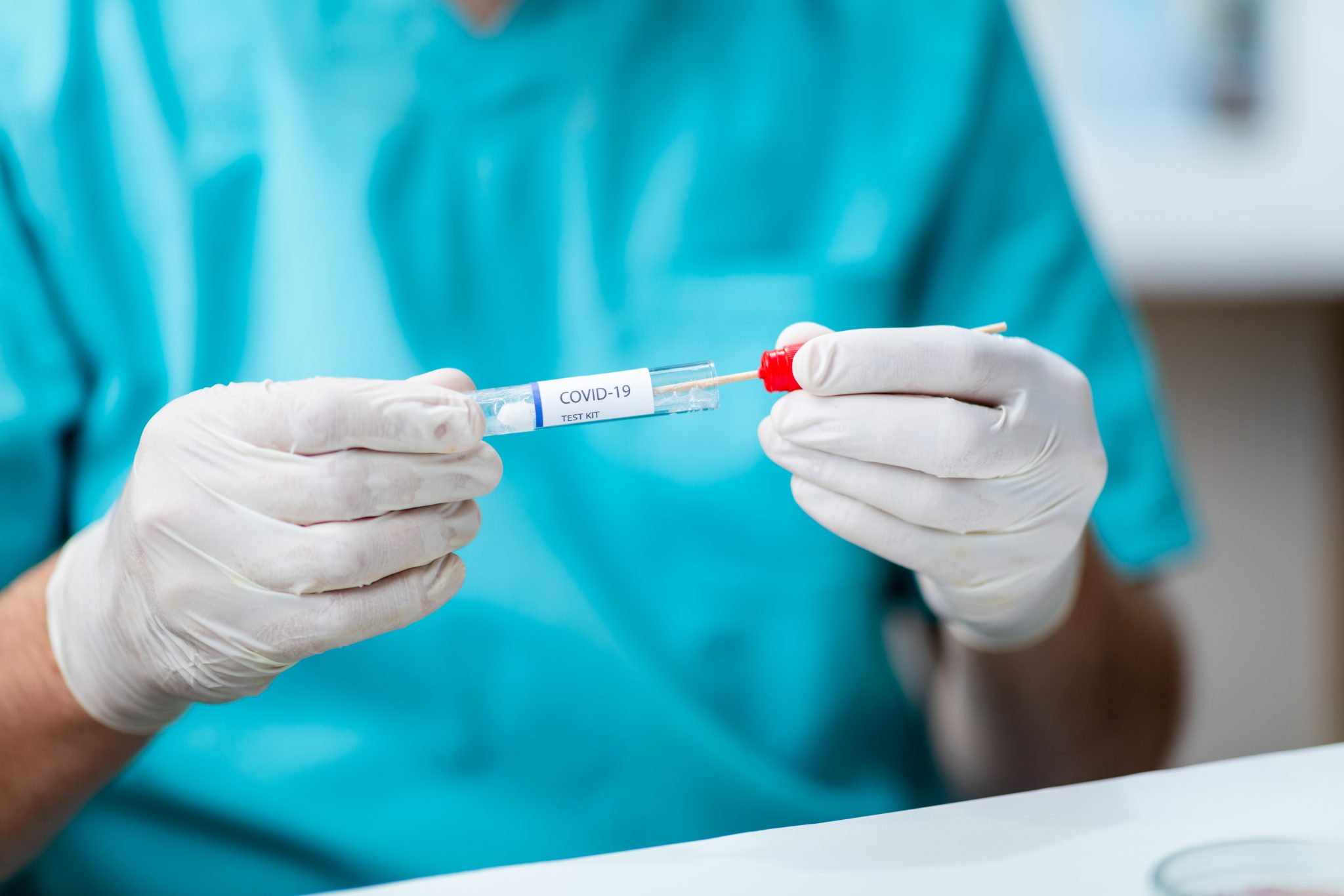 Hands in surgical gloves taking saliva sample on swab stick out of COVID-19 test kit